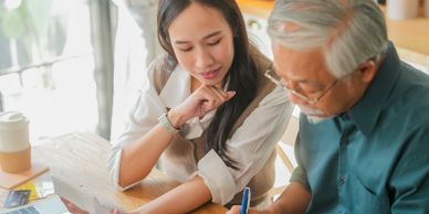 A young woman assisting an elderly man with paperwork at a kitchen table.