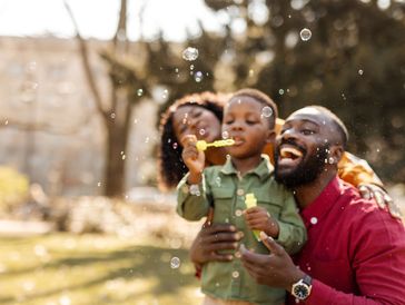 A joyful family blowing bubbles outdoors on a sunny day.