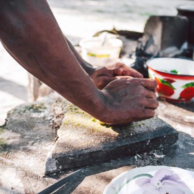 Hands crushing spices on a stone grinder outdoors.