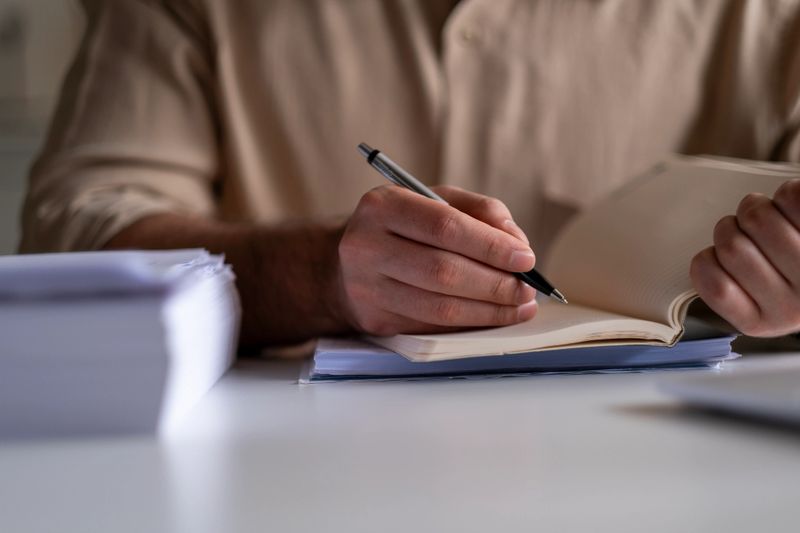 A close-up image of a man writing in a notebook with a pen at a desk, focusing on creativity and concentratio