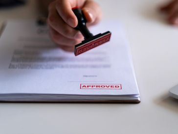 Hand stamping a document with an 'APPROVED' red stamp.