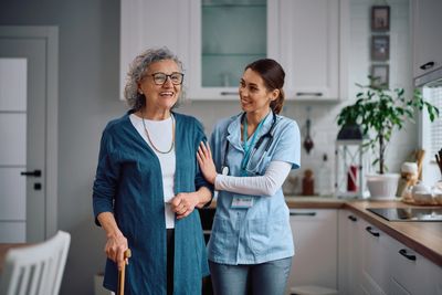 Nurse assisting elderly woman in a kitchen.