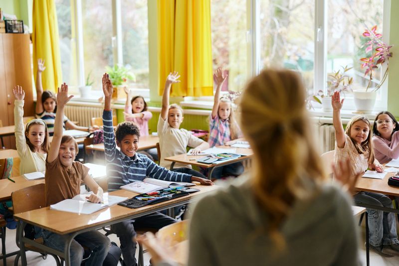 Group of happy students raising their hands to answer the teacher's question during a class at elementary school.