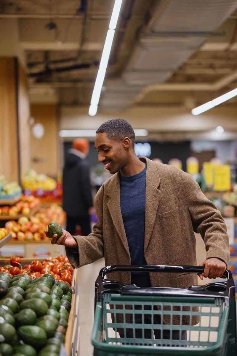 Happy black man buying fresh avocados at the supermarket.