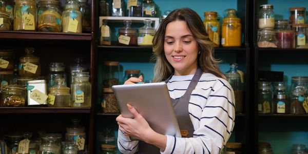 Smiling woman in apron using tablet in a spice shop.