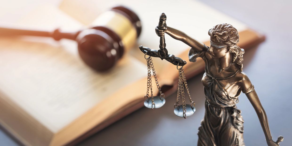 Statue of Lady Justice with book and gavel in the background.