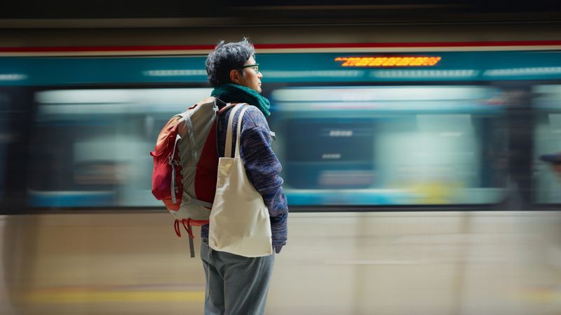 A man solo tourist is waiting the train to arrive at the station. He uses the public transportation to explore the city.