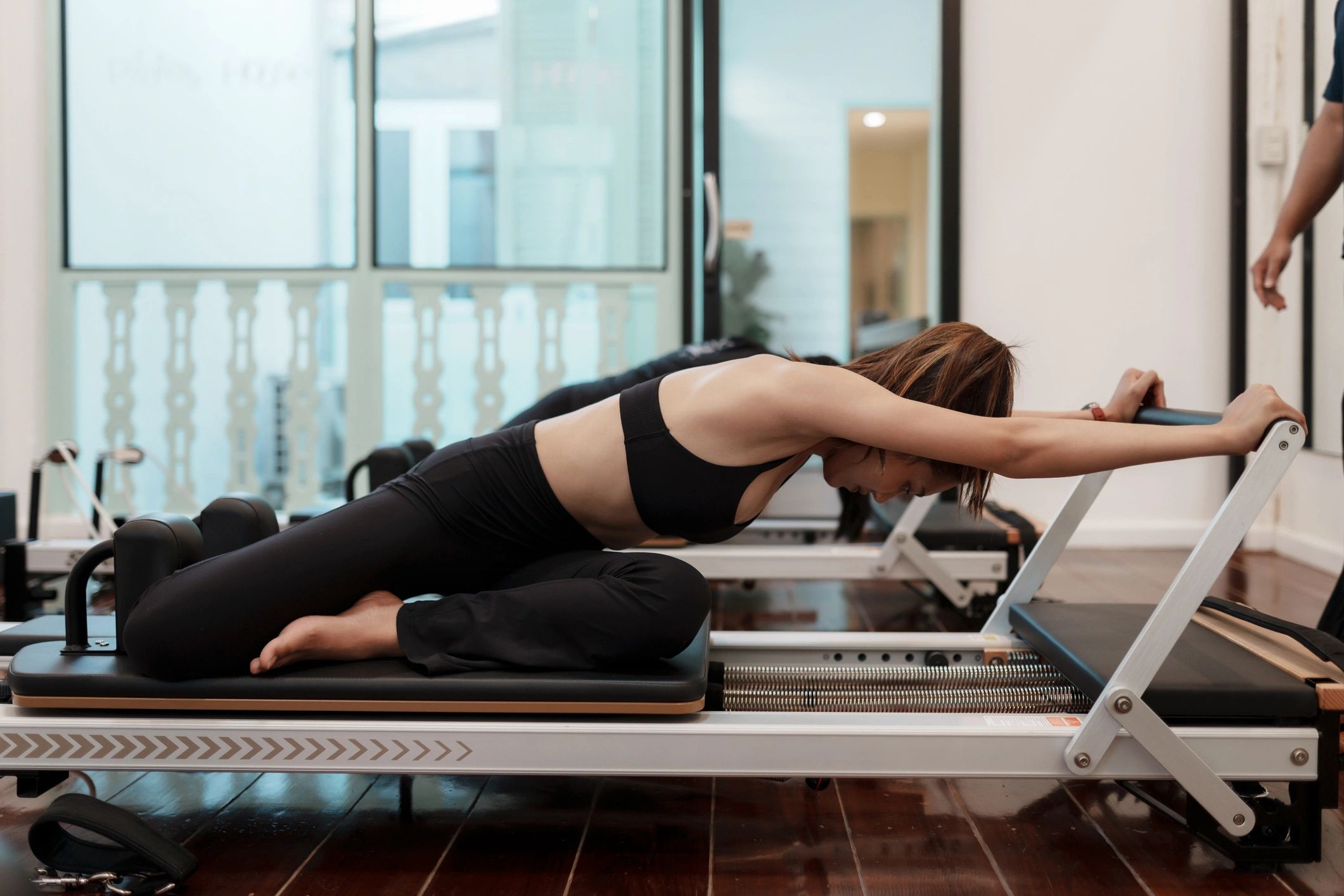 A woman stretching on a Pilates reformer in a gym.