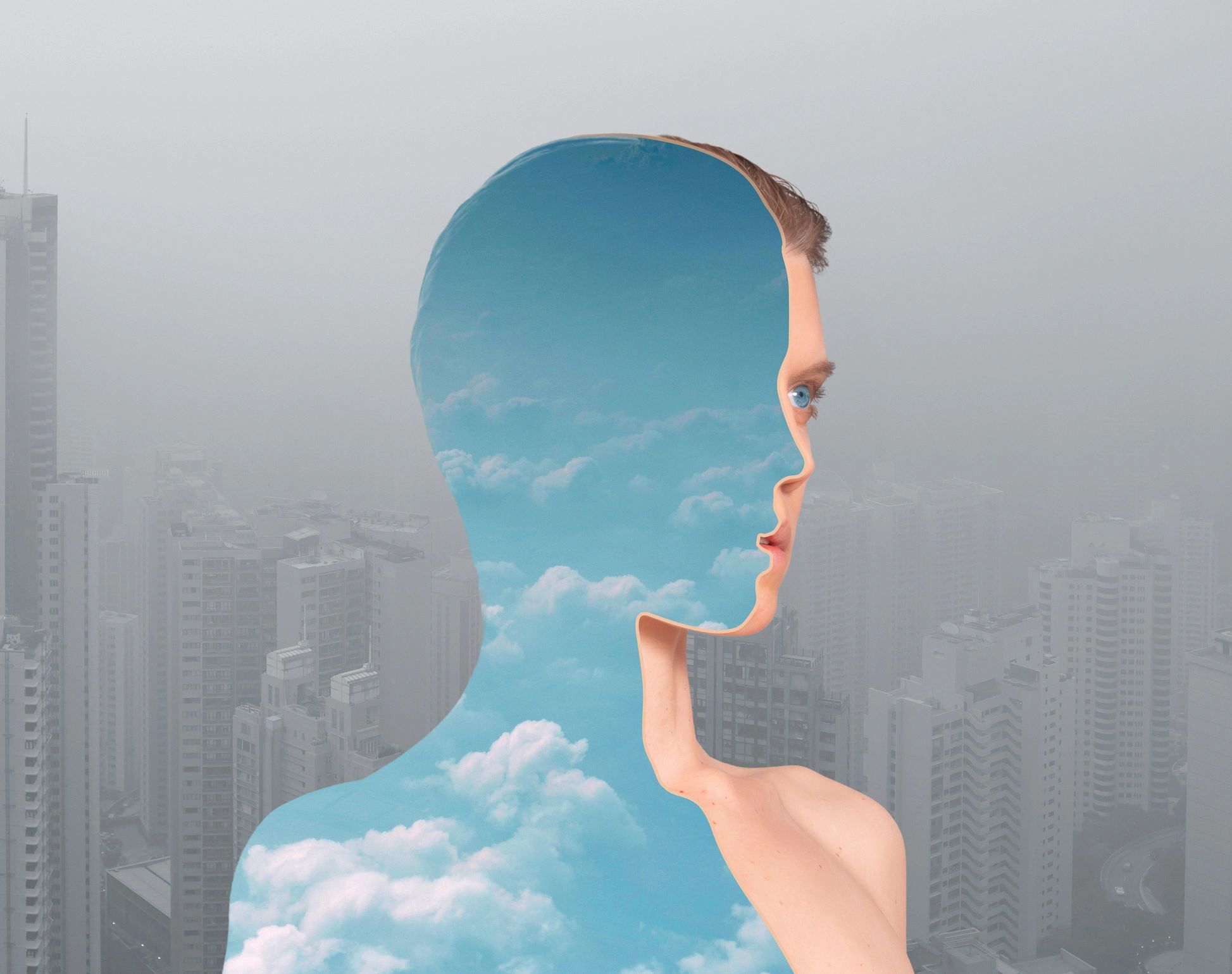 Surreal side profile with sky and clouds inside a human silhouette against a foggy city.
