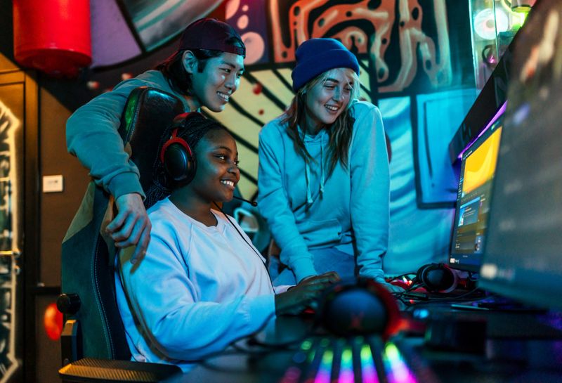 Three young adult gamers enjoying online video games while streaming in a vibrant, illuminated gaming room filled with colorful lights
