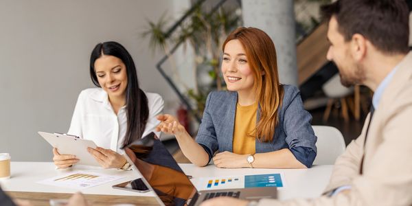 Three professionals discussing work with charts and tablets in a modern office.
