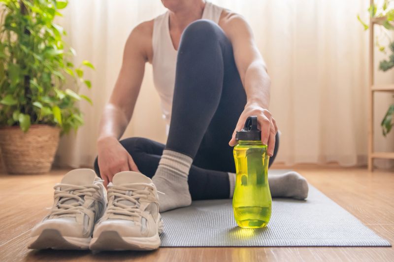 Mature woman relaxing on an exercise mat after completing a home workout, reaching for her electrolyte water bottle to stay hydrated and support her healthy lifestyle