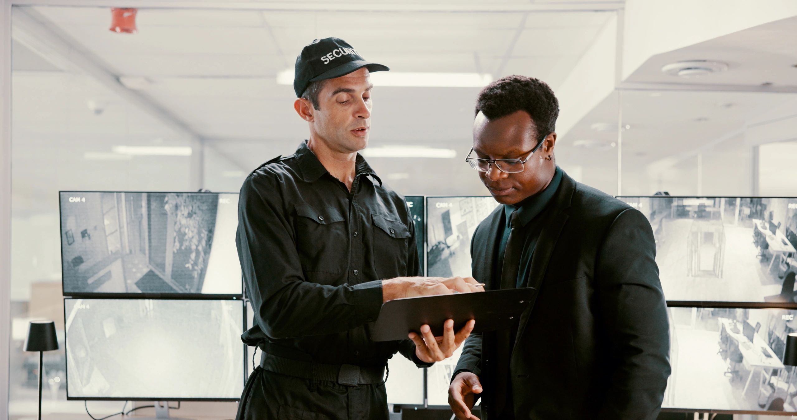 Two professionals discussing security operations in front of multiple CCTV monitors.