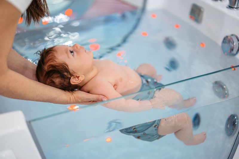 Mid-adult woman holding her baby boy while he is swimming in a tub in the baby spa.