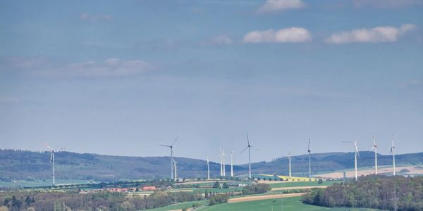 Wind turbines spread across rolling green hills under a partly cloudy sky.