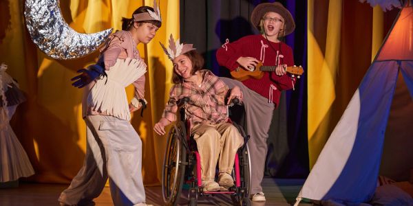 Children perform a play with costumes and wheelchair on stage.