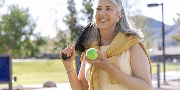 A Woman serves the wiffle ball in a recreational pickleball match.

