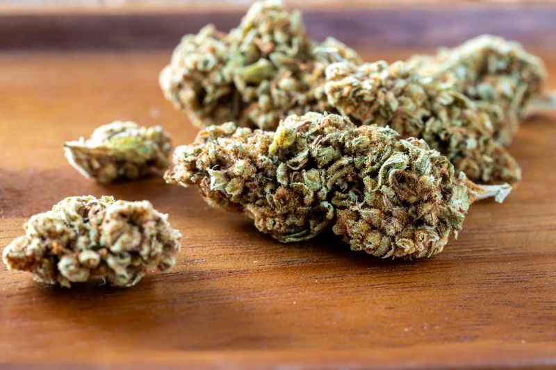 This image captures a close-up view of dried cannabis flower resting on a wooden tray. The vibrant green buds showcase rich textures and details, highlighting the natural quality of the plant.