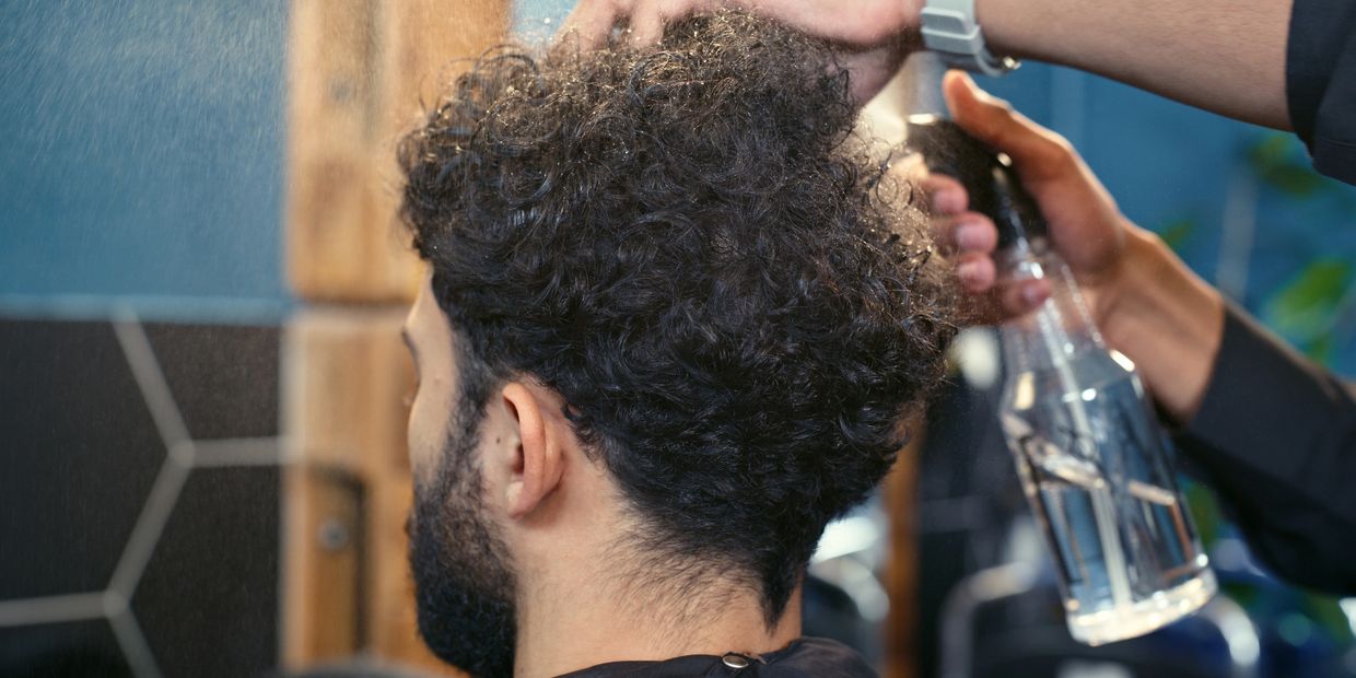 Man with curly hair getting sprayed with water.