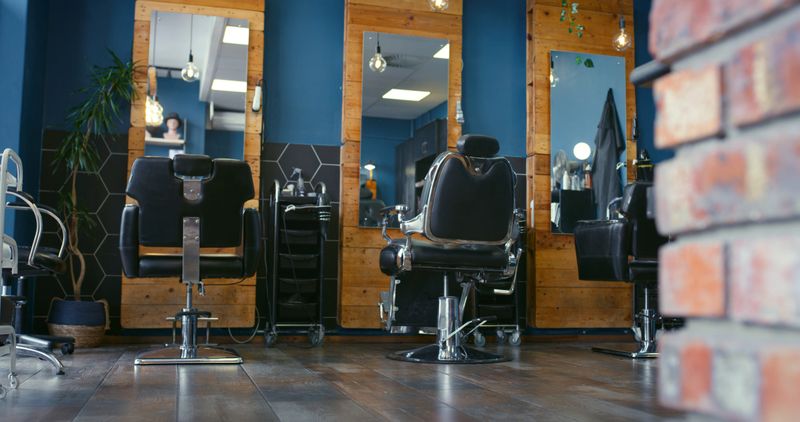 Barber, shop and chair with mirror in salon for hair care, grooming and beauty. Professional, business and furniture in room with cosmetics tools and equipment on shelf for hairdresser in store