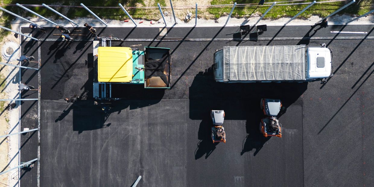 Construction workers and machinery paving a large asphalt surface.
