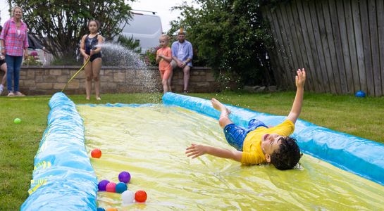 Boy sliding joyfully on a backyard slip and slide with colorful balls nearby.