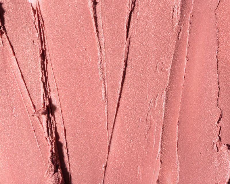 Close-up of smudged nude pink lipstick texture covering the entire frame. Creamy cosmetic smear with soft, matte finish. Beauty product background.
