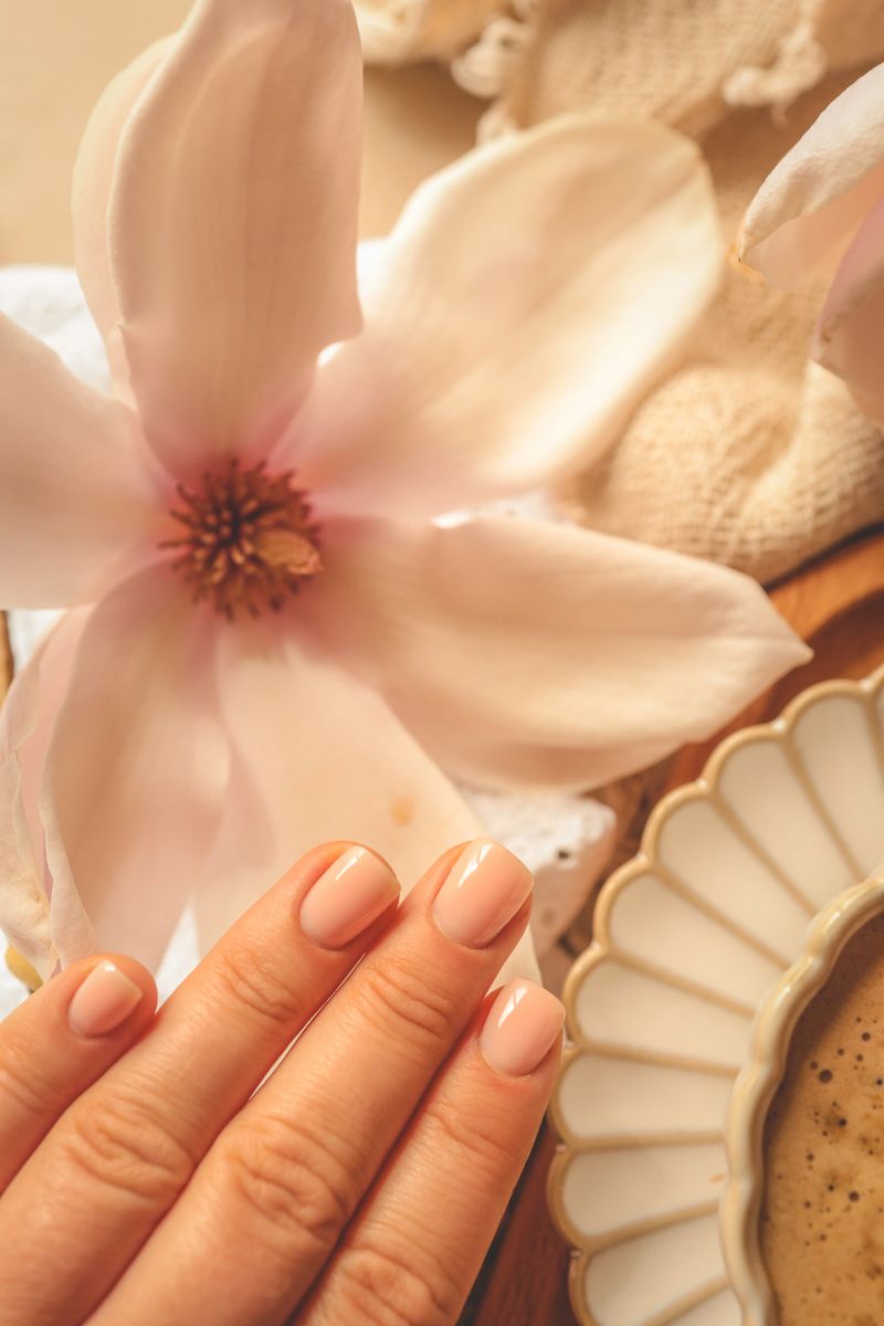 Close-up of nude manicure against a cozy spring scene with magnolia flowers and a cup of coffee on a wooden tray.