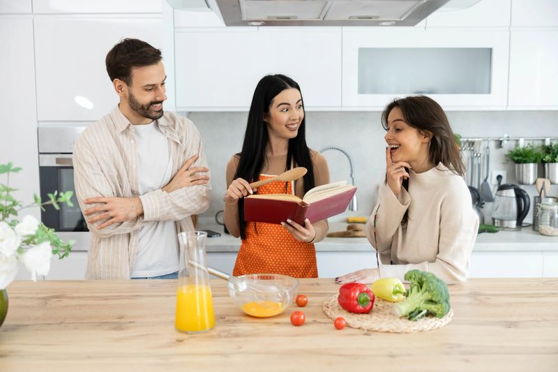 Three friends gather around a cookbook in a cozy kitchen, sharing laughs and ideas to create a delicious meal together.