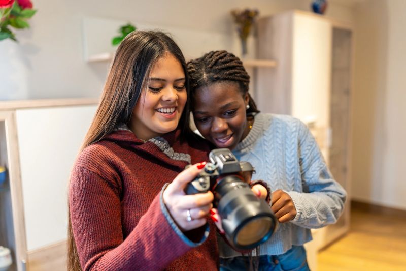 Two smiling teenage girls looking at photos on a digital camera, enjoying their time together