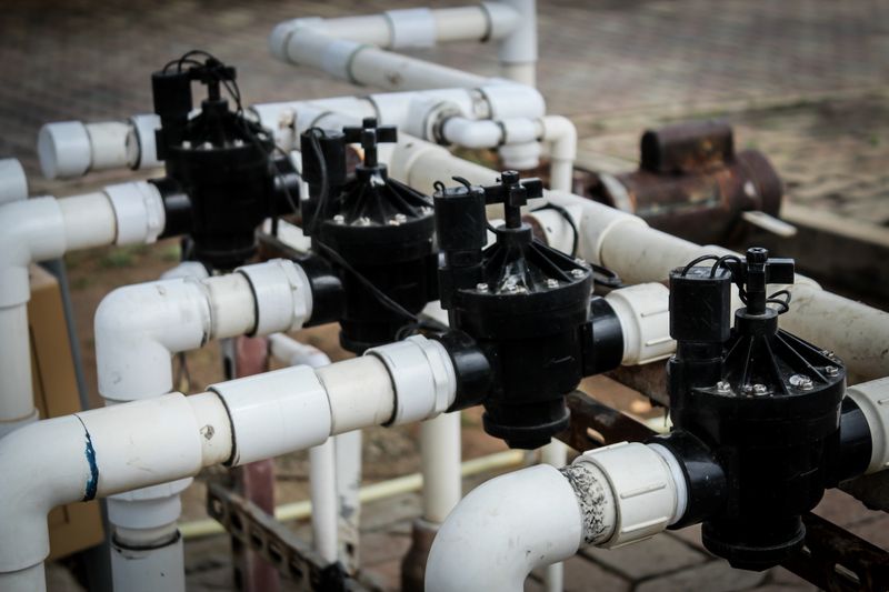 a close-up of a section of an irrigation system with white pvc pipes connected with fittings and black solenoid valves