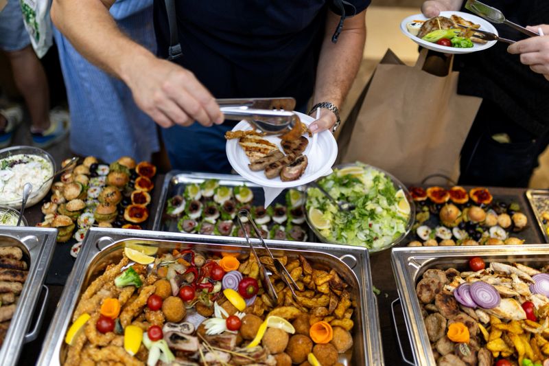 Guests select from an array of delicious foods at a lively festival. Tables are filled with grilled meats, fresh salads, and vibrant appetizers, creating a festive atmosphere.