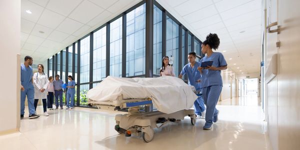 Medical staff and family escort a patient on a hospital stretcher through a bright hallway.