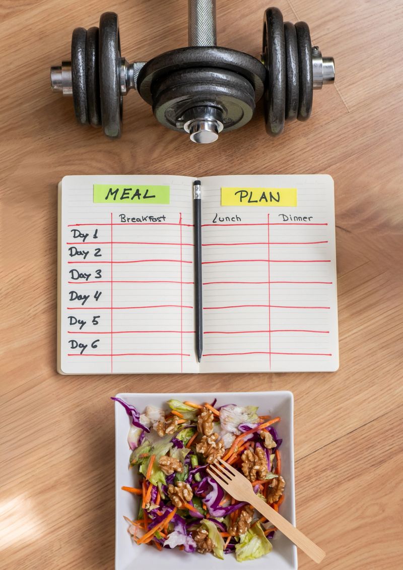 Woman is planning a balanced diet and workout routine, using a meal plan notebook, dumbbells, and a healthy salad for a comprehensive approach to fitness