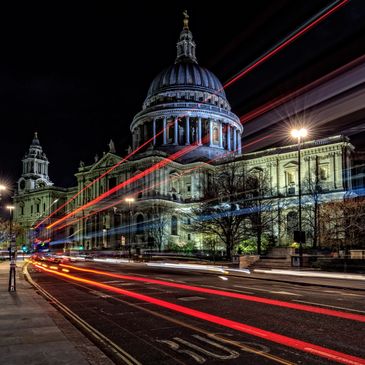 St. Paul's Cathedral illuminated at night with light trails from passing vehicles.