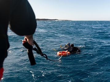 A person in the water is being helped by another from a boat with a rope and life buoy.