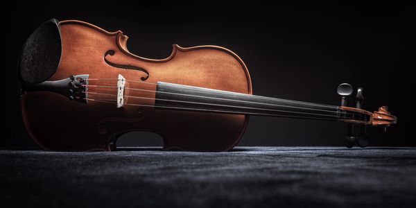 A violin lying on a dark textured surface with dramatic lighting.