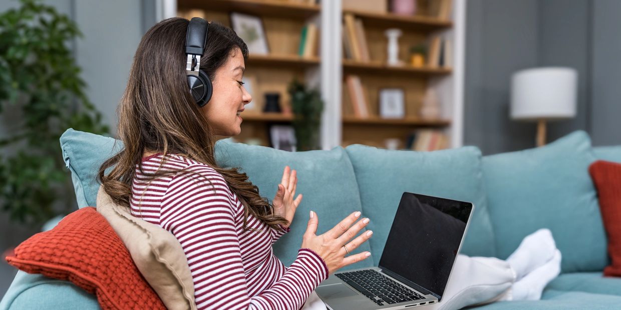 Woman with headphones video chatting on a laptop on a couch.