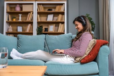 Woman working on laptop on sofa with headphones.