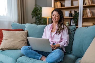 Woman smiling and using laptop on couch.