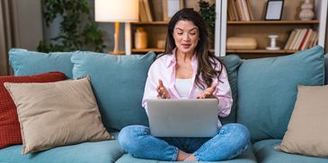 Woman sitting cross-legged on a couch, video chatting on a laptop.