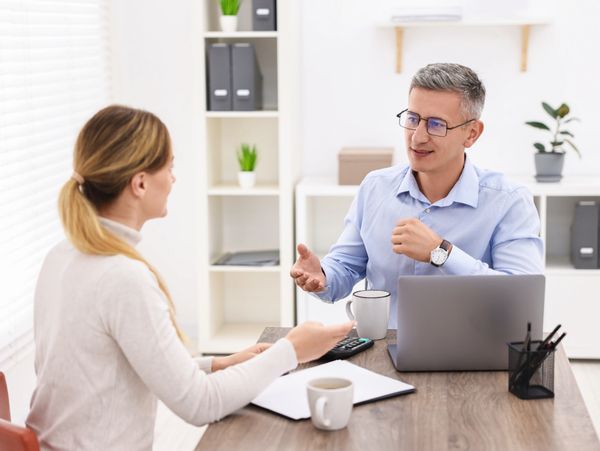 Two professionals discussing work at a desk with laptops and documents.