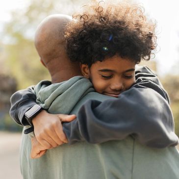 A child warmly hugs an adult outdoors, showing affection and comfort.
