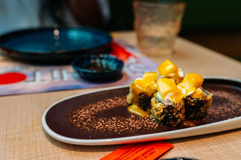 Delicious tempura uramaki sushi rolls, topped with fresh mango and creamy cheese, ready to be enjoyed in a vibrant restaurant setting