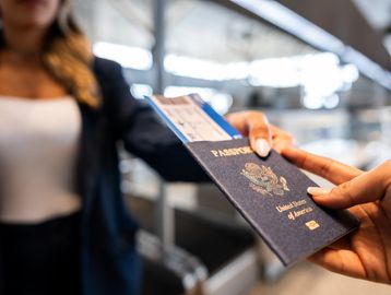 Person handing over a U.S. passport and boarding pass at an airport.
