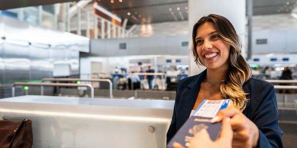 Smiling airport staff receiving a passport and boarding pass from a traveler.