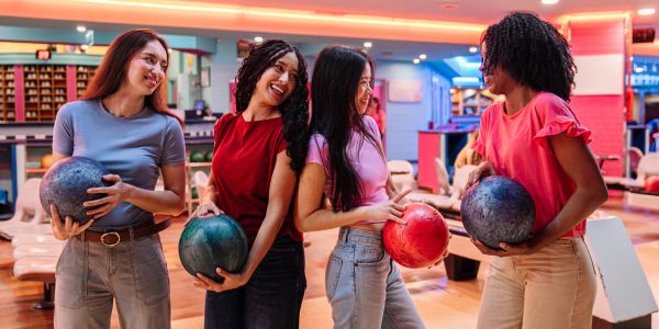 Four women holding bowling balls and smiling at a bowling alley.