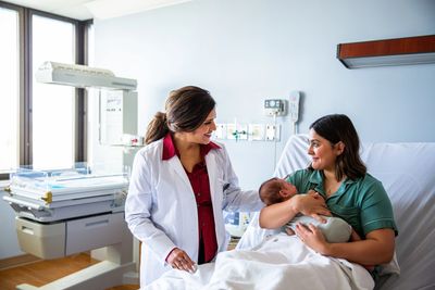 A doctor talks with a new mother holding her baby in a hospital room.