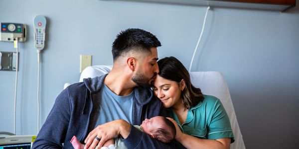 New parents lovingly embrace their newborn baby in a hospital room.