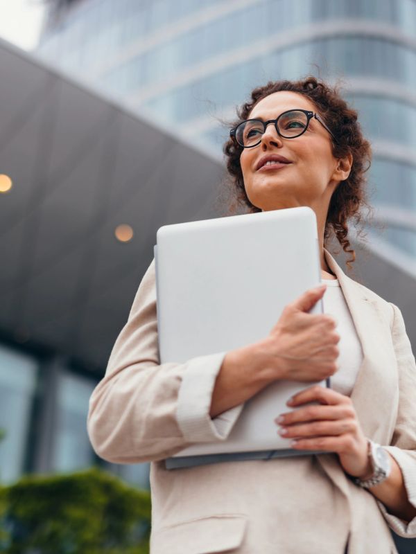 Confident woman holding a laptop outside an office building.